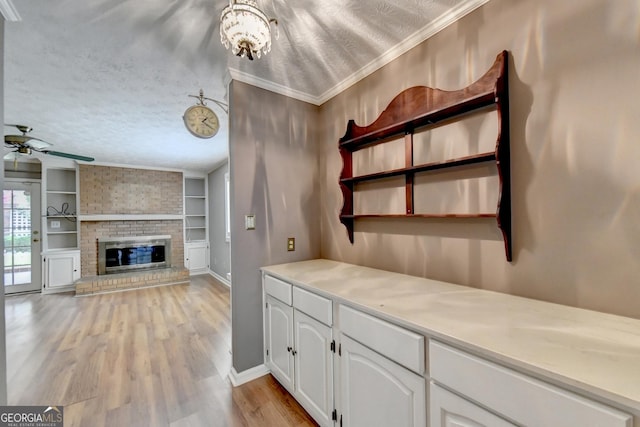 kitchen featuring ceiling fan with notable chandelier, white cabinets, built in features, ornamental molding, and a fireplace