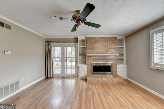 unfurnished living room featuring a textured ceiling, a wealth of natural light, a fireplace, built in features, and wood-type flooring