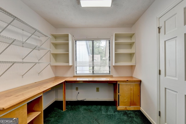 unfurnished office with a textured ceiling, dark colored carpet, and built in desk