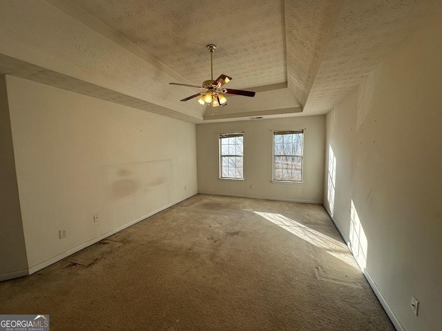 unfurnished room featuring ceiling fan, light carpet, a textured ceiling, and a tray ceiling