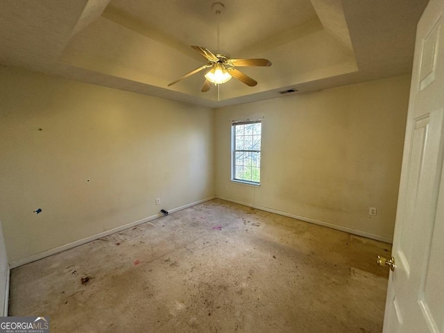 empty room with ceiling fan and a tray ceiling