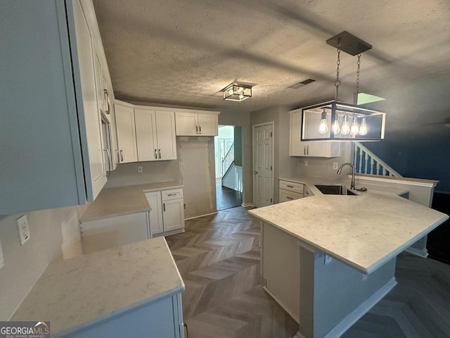 kitchen featuring sink, white cabinets, a textured ceiling, and hanging light fixtures