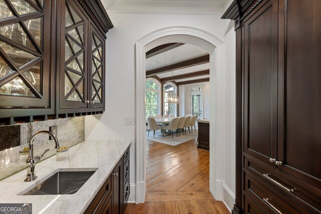 bar with sink, dark brown cabinets, and light stone counters