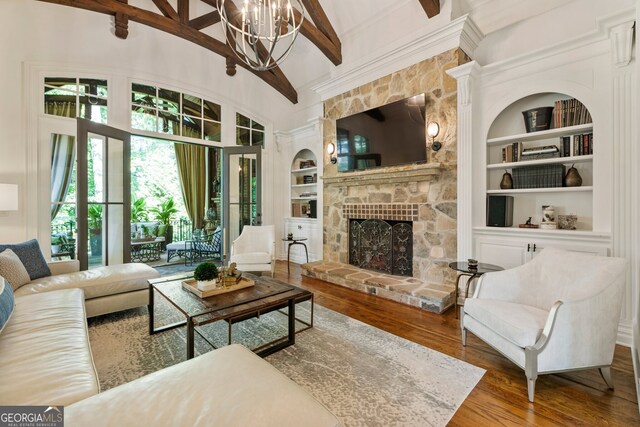 living room with hardwood / wood-style flooring, a chandelier, beam ceiling, built in features, and a stone fireplace