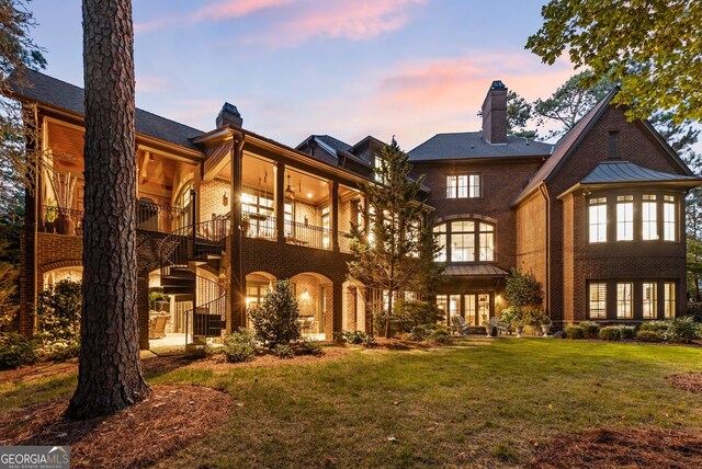 back house at dusk with a balcony and a yard