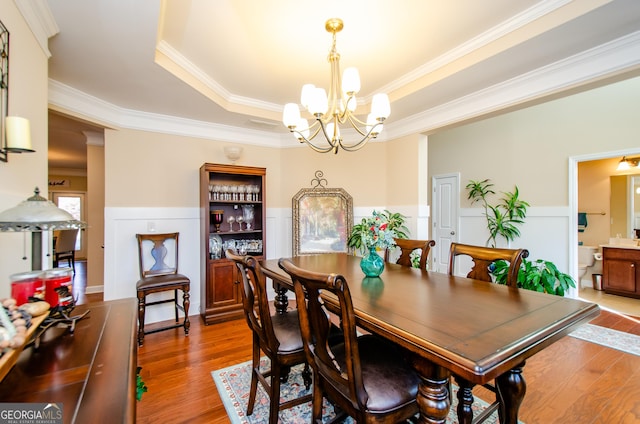 dining space featuring wood-type flooring, a raised ceiling, ornamental molding, and a notable chandelier