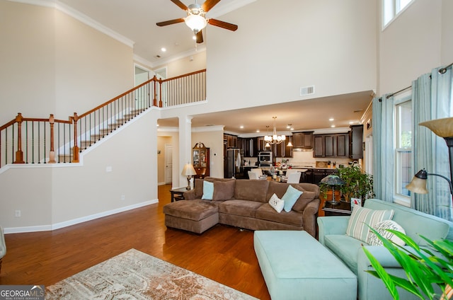 living room featuring a towering ceiling, crown molding, dark hardwood / wood-style flooring, and ceiling fan with notable chandelier