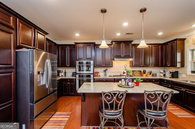 kitchen with a center island, light wood-type flooring, dark brown cabinetry, pendant lighting, and appliances with stainless steel finishes