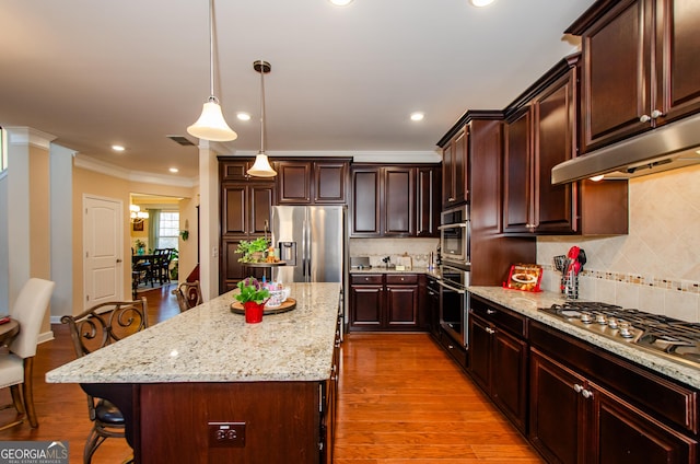 kitchen with appliances with stainless steel finishes, a center island, ornamental molding, a kitchen bar, and decorative light fixtures