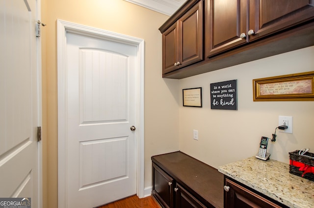 interior space featuring light wood-type flooring, crown molding, light stone countertops, and dark brown cabinetry