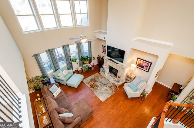 living room with a towering ceiling, ceiling fan, a wealth of natural light, and a stone fireplace