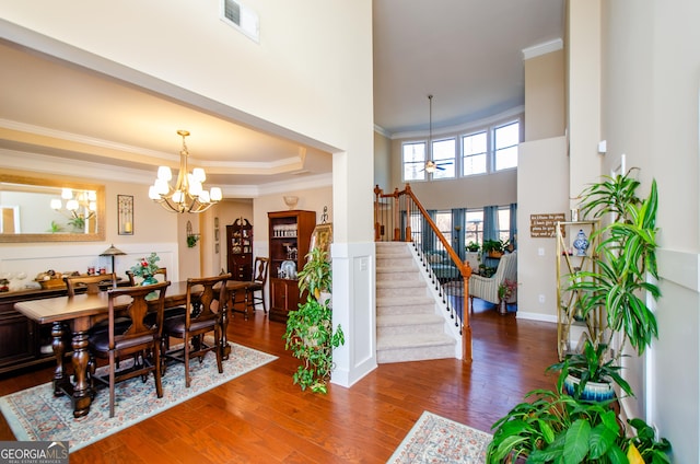 dining area with ornamental molding, dark wood-type flooring, a towering ceiling, and ceiling fan with notable chandelier