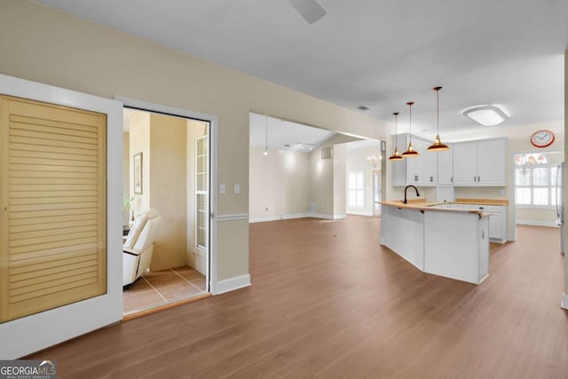 kitchen featuring pendant lighting, a center island with sink, white cabinets, wood-type flooring, and sink