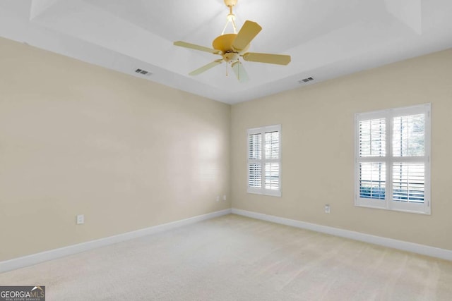 carpeted empty room with ceiling fan and a tray ceiling