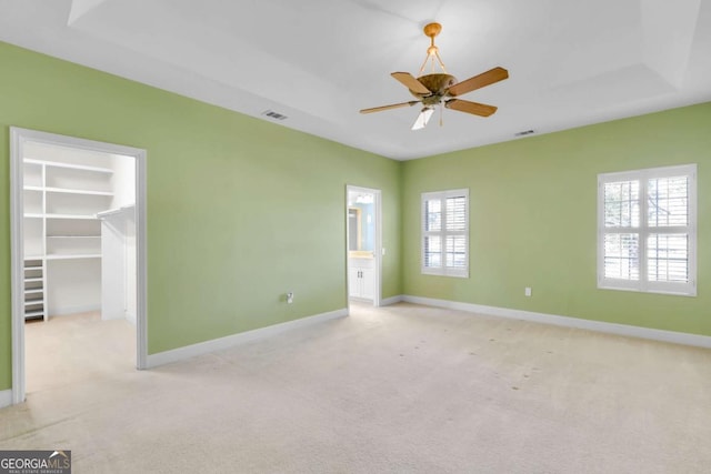 unfurnished bedroom with a raised ceiling, ceiling fan, a spacious closet, and multiple windows