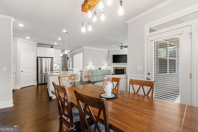 dining space featuring dark hardwood / wood-style floors, crown molding, a fireplace, ceiling fan, and sink