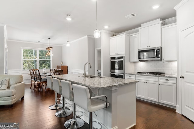 kitchen featuring stainless steel appliances, sink, decorative light fixtures, light stone countertops, and a kitchen island with sink