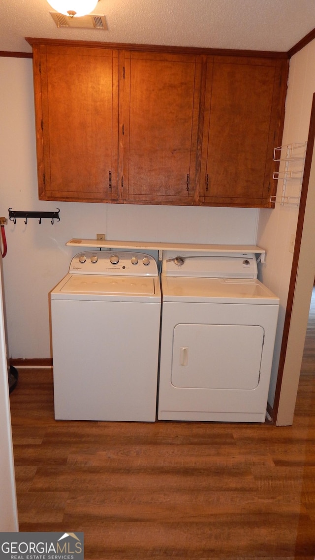 clothes washing area featuring washer and dryer, cabinets, a textured ceiling, and wood-type flooring