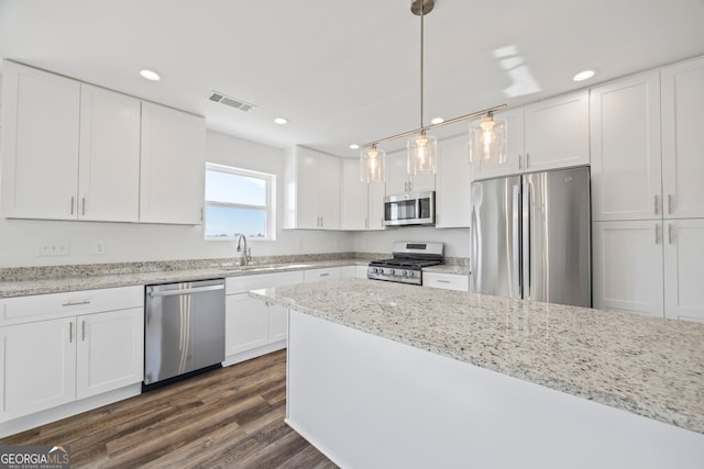 kitchen with stainless steel appliances, pendant lighting, light stone counters, white cabinets, and sink