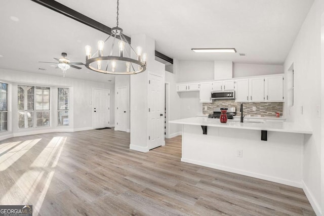 kitchen featuring pendant lighting, stainless steel appliances, lofted ceiling, white cabinets, and a kitchen breakfast bar