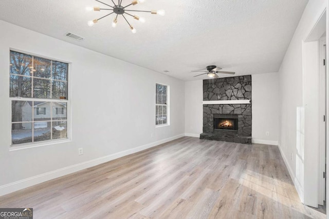 unfurnished living room featuring a textured ceiling, light hardwood / wood-style flooring, and a stone fireplace