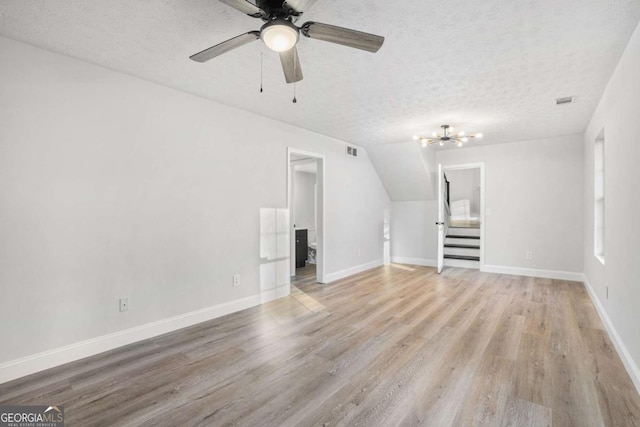 unfurnished living room with a textured ceiling, ceiling fan, light wood-type flooring, and vaulted ceiling