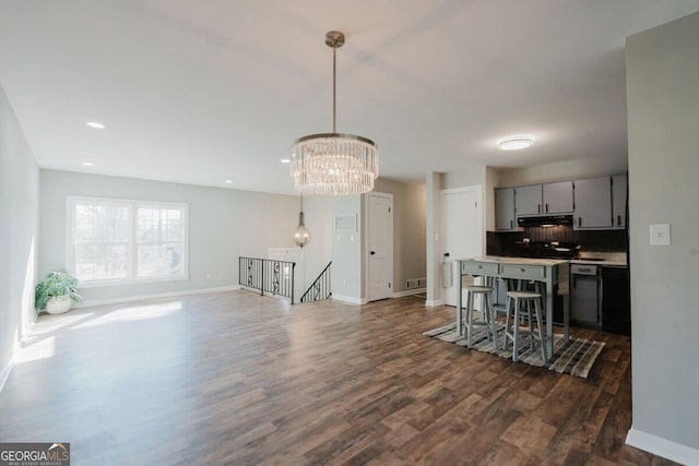 kitchen with baseboards, dark wood-style flooring, gray cabinetry, under cabinet range hood, and backsplash