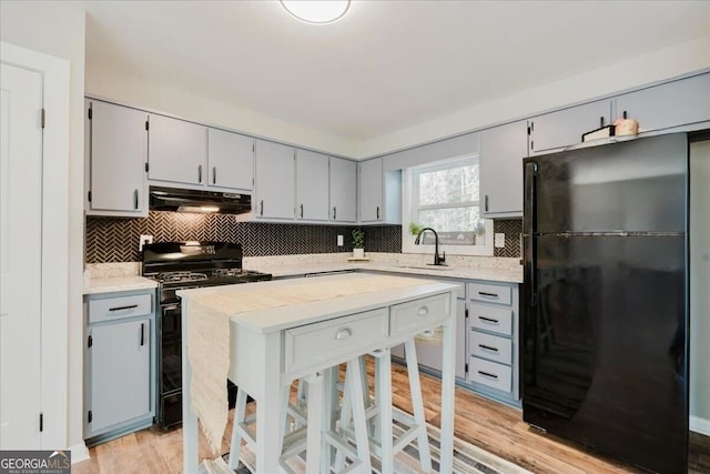 kitchen with gray cabinetry, a sink, under cabinet range hood, and black appliances