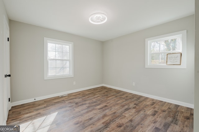 unfurnished room featuring visible vents, plenty of natural light, baseboards, and wood finished floors