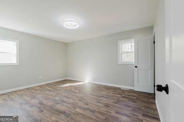 unfurnished room featuring dark wood-type flooring, visible vents, and baseboards