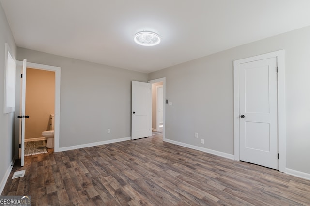 unfurnished bedroom with connected bathroom, wood finished floors, visible vents, and baseboards