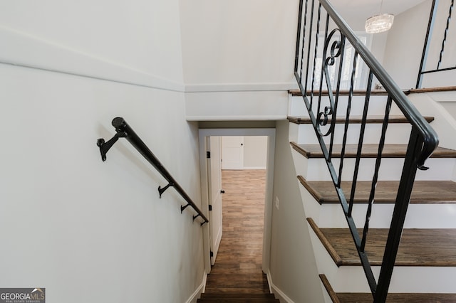 stairs with wood finished floors and an inviting chandelier