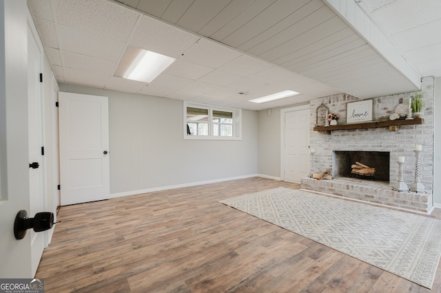 unfurnished living room featuring a brick fireplace, wood finished floors, a paneled ceiling, and baseboards