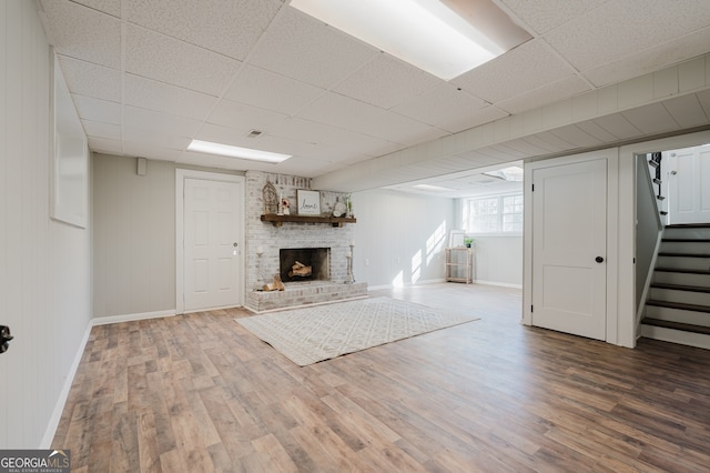 unfurnished living room with stairs, a brick fireplace, wood finished floors, and a paneled ceiling