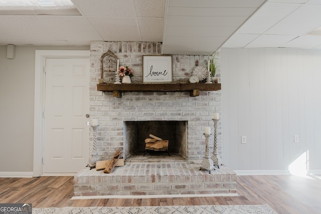 details featuring a drop ceiling, a brick fireplace, wood finished floors, and baseboards