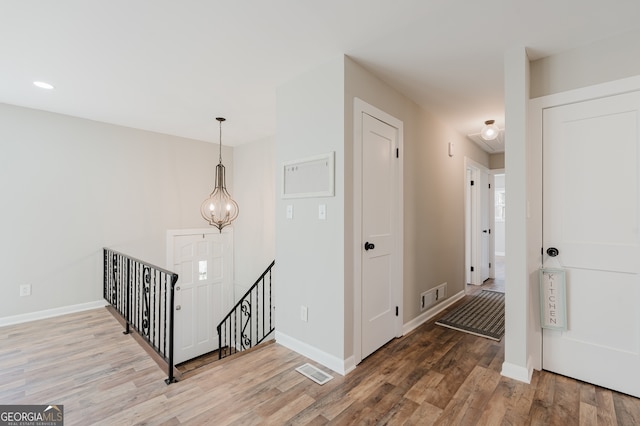 hallway featuring visible vents, wood finished floors, an upstairs landing, and baseboards