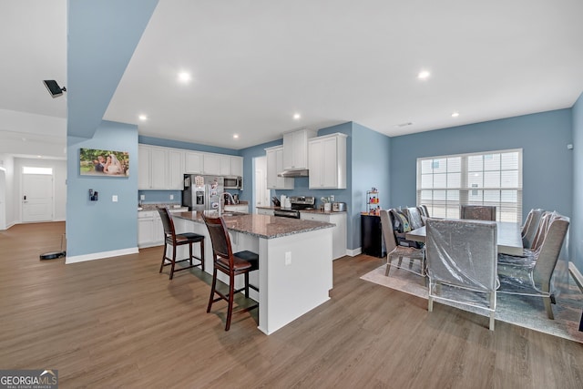 kitchen featuring appliances with stainless steel finishes, light hardwood / wood-style floors, white cabinets, and a kitchen island with sink