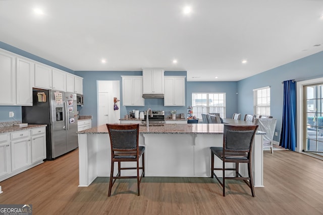 kitchen with a kitchen island with sink, a breakfast bar, and white cabinetry