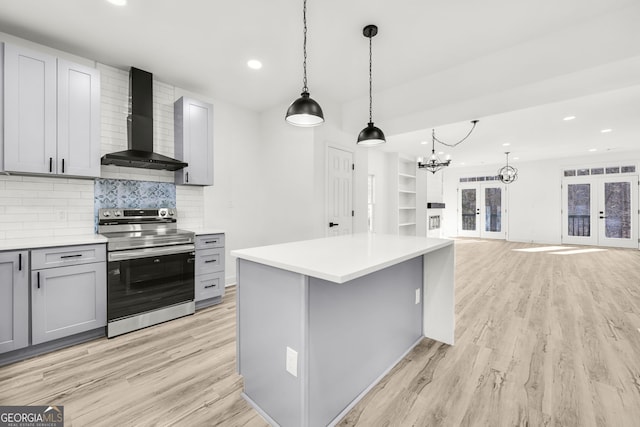 kitchen featuring french doors, stainless steel electric range oven, hanging light fixtures, gray cabinets, and wall chimney range hood