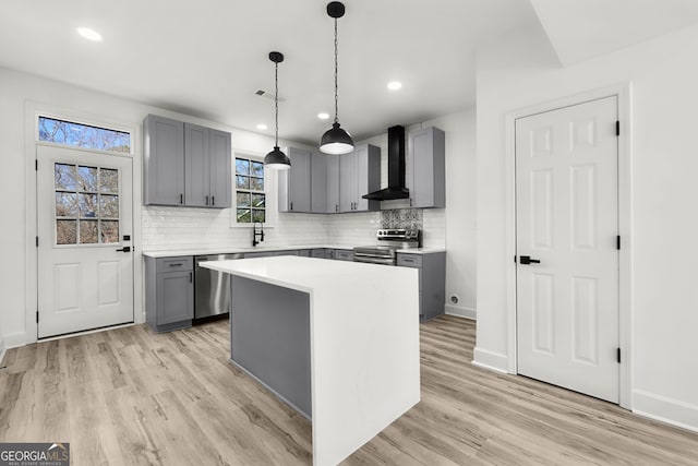 kitchen featuring stainless steel appliances, wall chimney range hood, gray cabinetry, and a center island