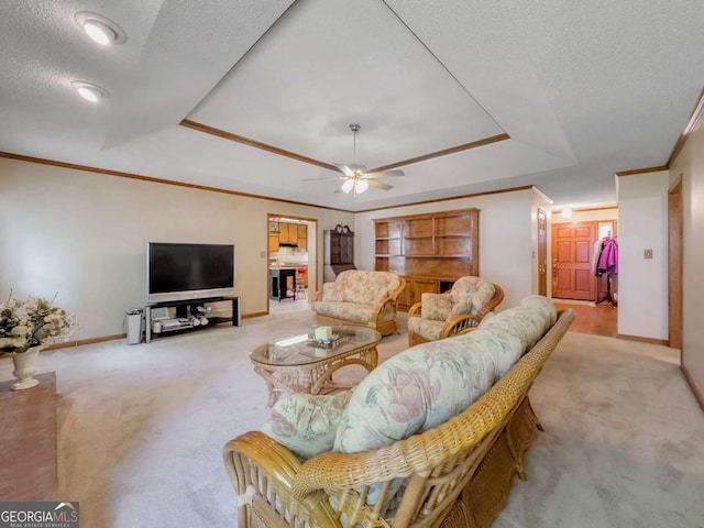 living room featuring ceiling fan, light carpet, ornamental molding, and a tray ceiling