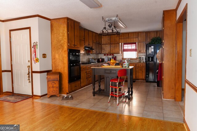 kitchen featuring a textured ceiling, a center island, black appliances, and light tile patterned floors