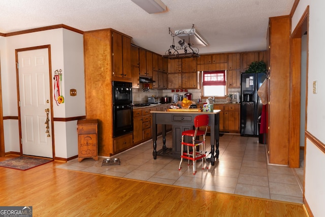 114 Tracy Ln, Mcdonough, GA 30253 - kitchen with black appliances, brown cabinetry, under cabinet range hood, a textured ceiling, and crown molding