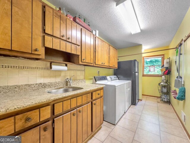 clothes washing area featuring sink, a textured ceiling, independent washer and dryer, and light tile patterned floors