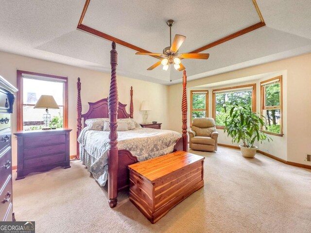 bedroom with a textured ceiling, ceiling fan, a tray ceiling, and carpet flooring