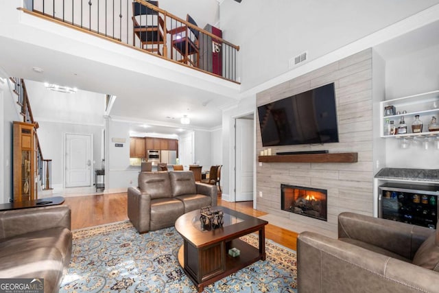 living room featuring a towering ceiling, a tile fireplace, ornamental molding, and hardwood / wood-style flooring