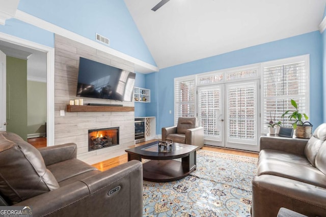 living room featuring lofted ceiling, crown molding, ceiling fan, wood-type flooring, and a stone fireplace