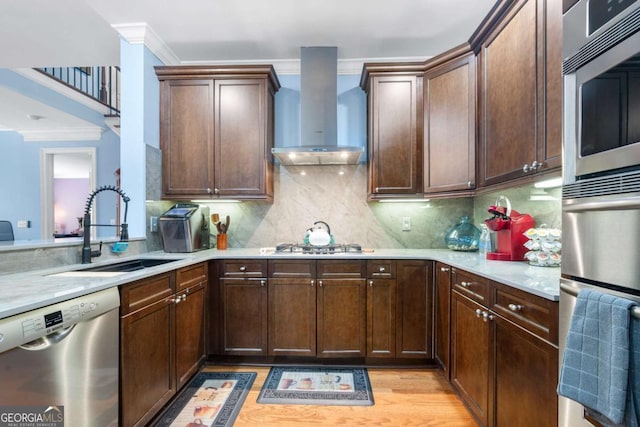 kitchen with appliances with stainless steel finishes, wall chimney exhaust hood, sink, dark brown cabinets, and backsplash