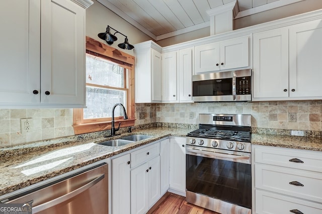 kitchen featuring light stone countertops, tasteful backsplash, white cabinets, appliances with stainless steel finishes, and sink