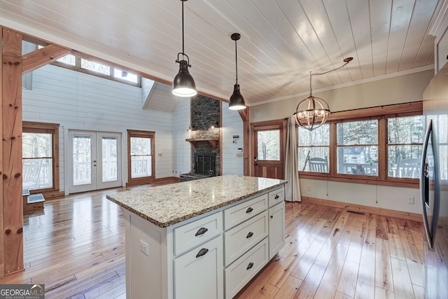 kitchen featuring light stone counters, white cabinets, light wood-type flooring, and hanging light fixtures